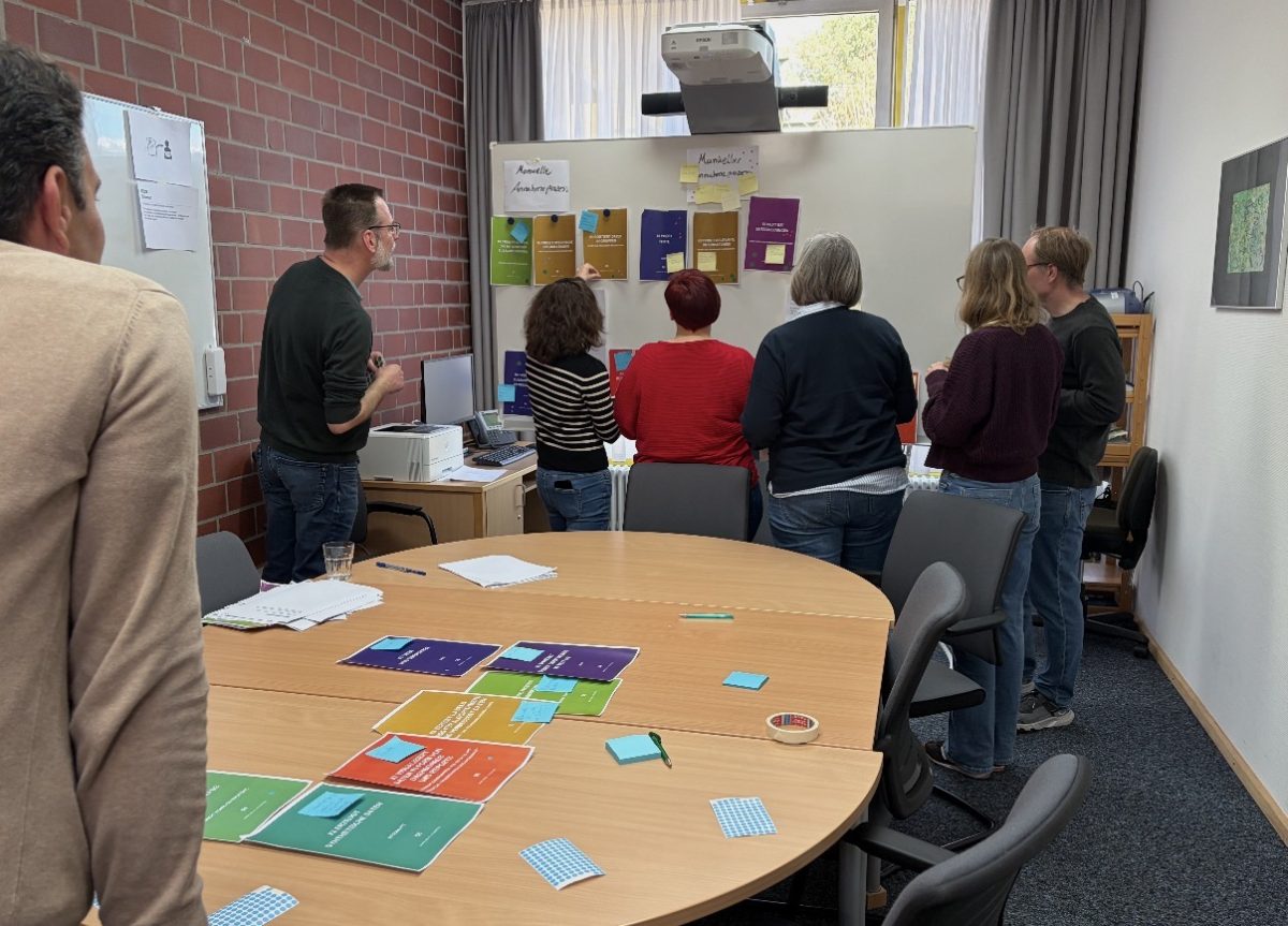 Team in einem Besprechungsraum bei einem Workshop mit Moderationskarten an der Wand.